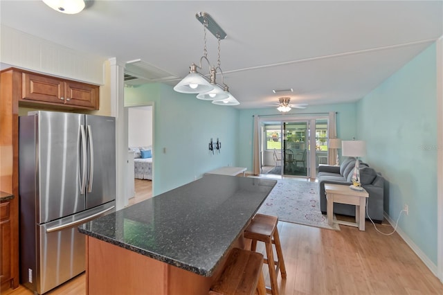 kitchen featuring open floor plan, brown cabinets, freestanding refrigerator, a center island, and decorative light fixtures