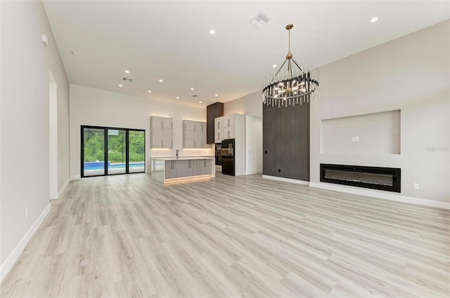 unfurnished living room with a high ceiling, a chandelier, and light wood-type flooring