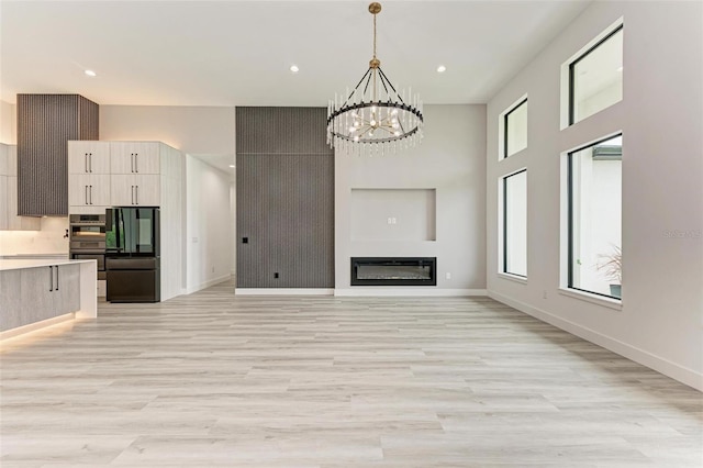 unfurnished living room featuring an inviting chandelier, a high ceiling, and light wood-type flooring