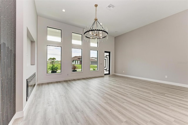 unfurnished living room with a healthy amount of sunlight, an inviting chandelier, light hardwood / wood-style floors, and a towering ceiling