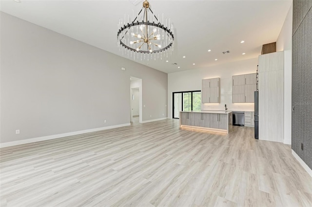 unfurnished living room with a towering ceiling, sink, a chandelier, and light hardwood / wood-style flooring