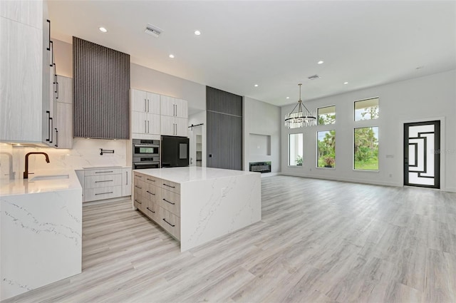 kitchen featuring light stone counters, a large island, sink, and hanging light fixtures