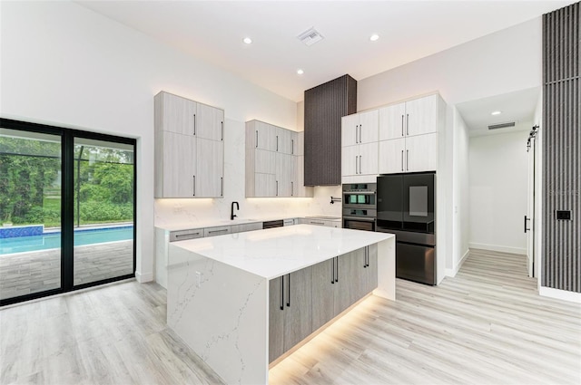 kitchen featuring sink, double wall oven, light stone countertops, light hardwood / wood-style floors, and a kitchen island