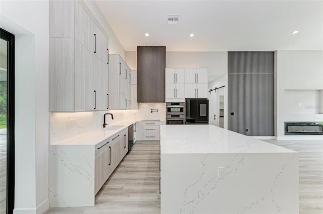 kitchen featuring a kitchen island, dishwasher, sink, fridge, and light stone counters