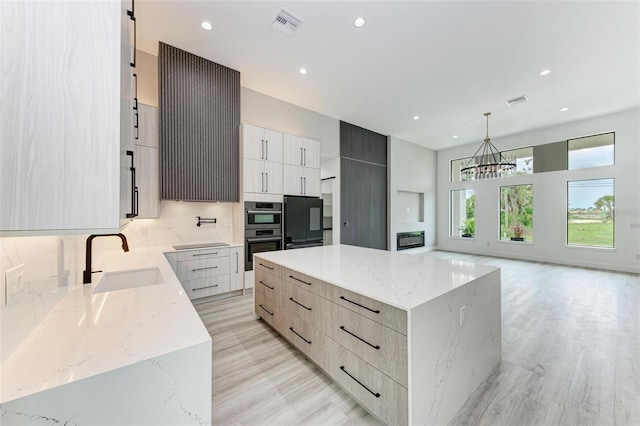 kitchen featuring decorative light fixtures, sink, fridge, light stone countertops, and a spacious island