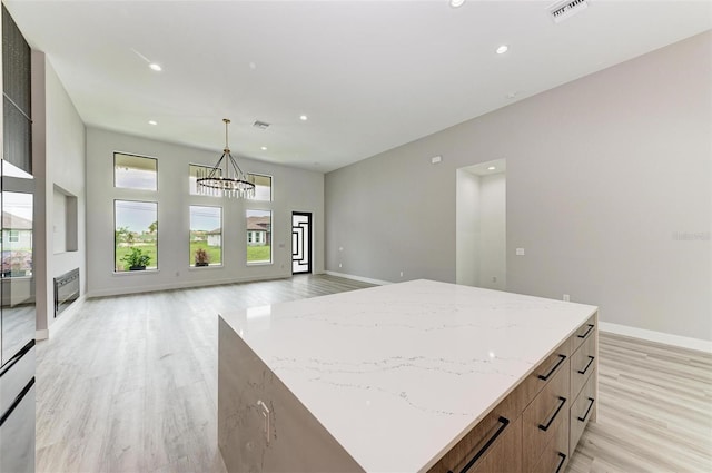 kitchen featuring pendant lighting, an inviting chandelier, a center island, light stone counters, and light hardwood / wood-style floors