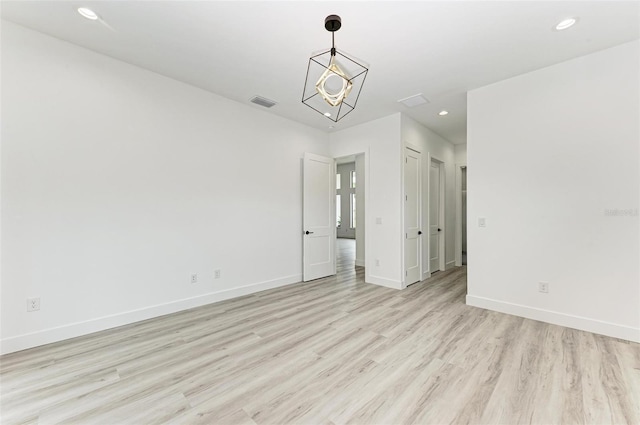 unfurnished room featuring an inviting chandelier and light hardwood / wood-style flooring