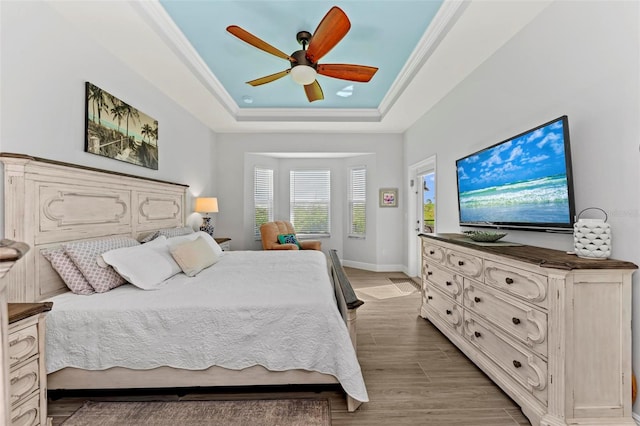 bedroom with wood-type flooring, a tray ceiling, ceiling fan, and ornamental molding