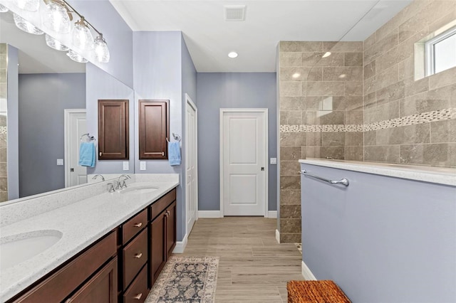 bathroom featuring hardwood / wood-style flooring, vanity, and tiled shower