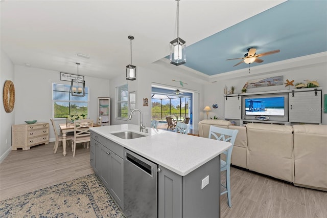 kitchen with gray cabinetry, dishwasher, a center island with sink, sink, and decorative light fixtures