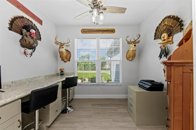 home office with light wood-type flooring, built in desk, and ceiling fan