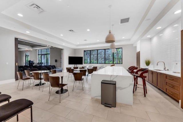 interior space with pendant lighting, light tile patterned floors, a tray ceiling, sink, and light stone counters