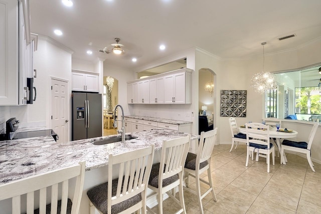 kitchen featuring stainless steel refrigerator with ice dispenser, white cabinetry, sink, hanging light fixtures, and stove