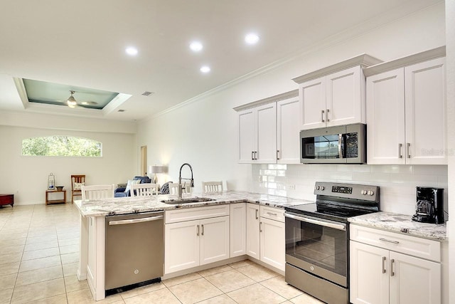 kitchen with a sink, stainless steel appliances, decorative backsplash, a peninsula, and ornamental molding
