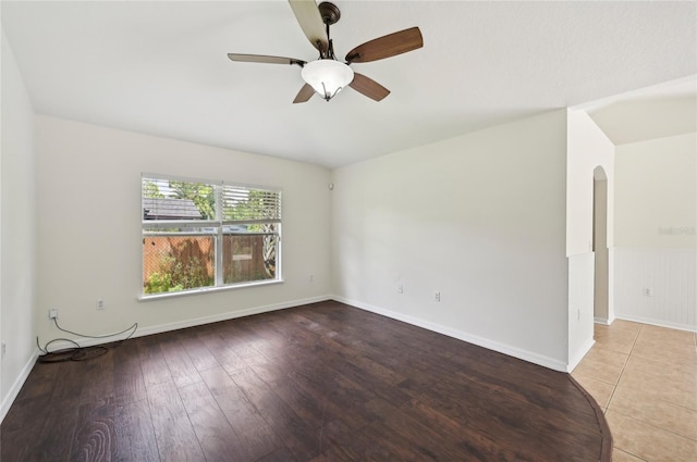 empty room featuring arched walkways, ceiling fan, baseboards, light wood-style floors, and wainscoting