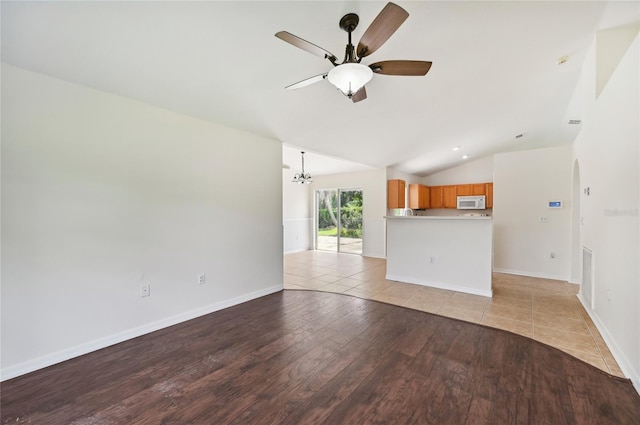 unfurnished living room with ceiling fan with notable chandelier, light wood-type flooring, and vaulted ceiling