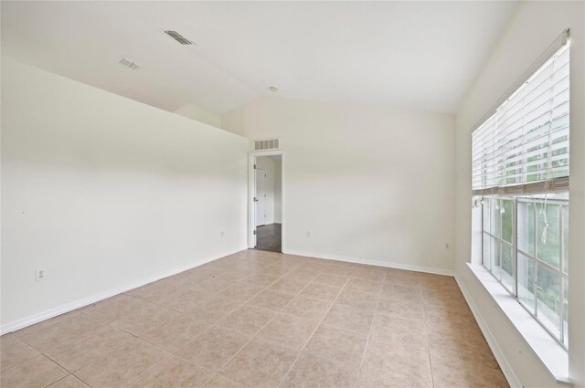 unfurnished room with lofted ceiling, light tile patterned floors, and a healthy amount of sunlight