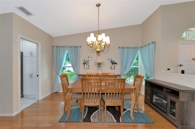 dining space with vaulted ceiling, a healthy amount of sunlight, a chandelier, and light hardwood / wood-style flooring