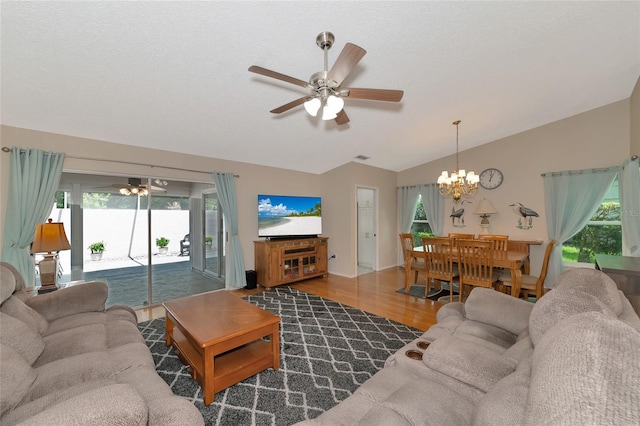 living room with hardwood / wood-style flooring, a healthy amount of sunlight, lofted ceiling, and ceiling fan with notable chandelier