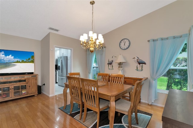 dining room with a chandelier, vaulted ceiling, and light hardwood / wood-style flooring