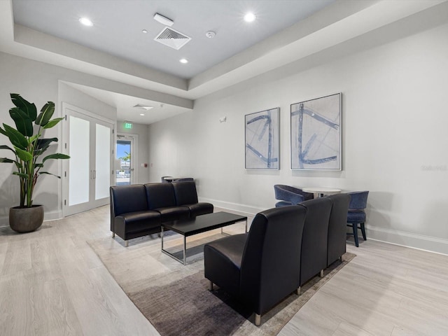 living room with light hardwood / wood-style flooring, a tray ceiling, and french doors