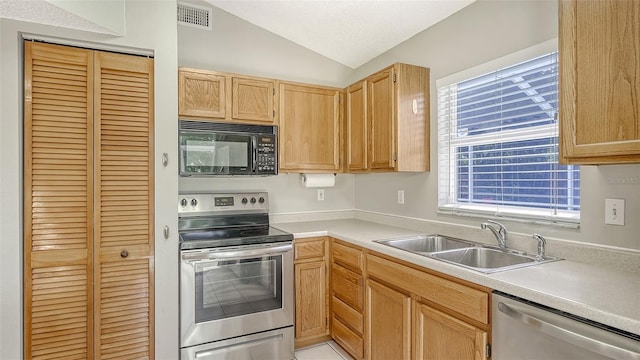 kitchen with appliances with stainless steel finishes, vaulted ceiling, sink, and light brown cabinetry