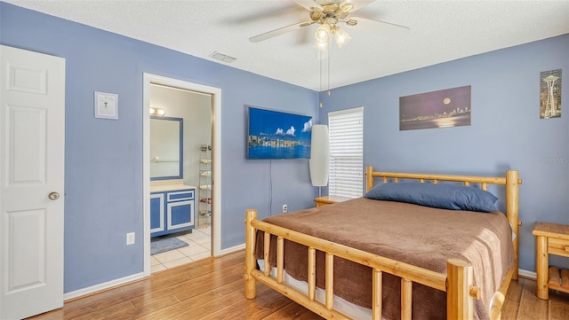 bedroom featuring ceiling fan, ensuite bathroom, light hardwood / wood-style flooring, and a textured ceiling