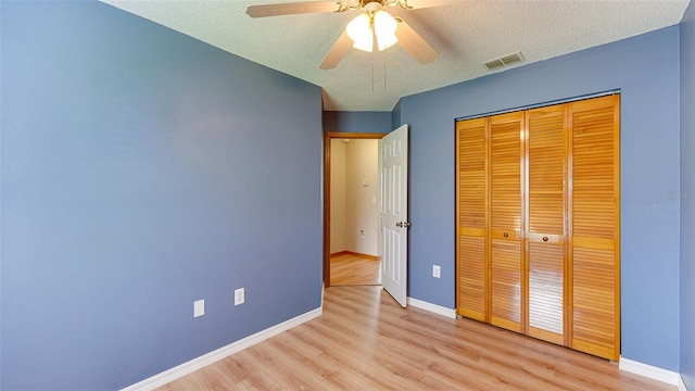 unfurnished bedroom featuring ceiling fan, a closet, light hardwood / wood-style floors, and a textured ceiling