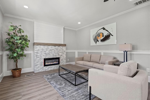 living room with ceiling fan, a stone fireplace, crown molding, and hardwood / wood-style flooring