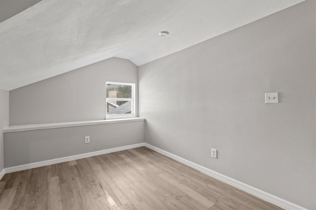 additional living space with lofted ceiling, a textured ceiling, and light hardwood / wood-style floors