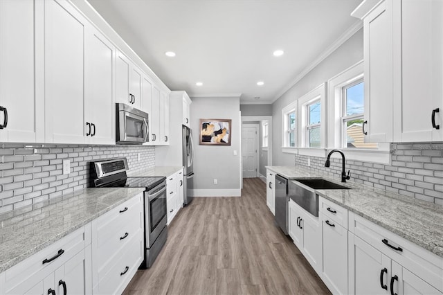 kitchen featuring appliances with stainless steel finishes, white cabinets, light stone countertops, and sink