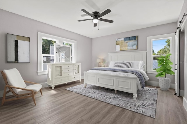 bedroom featuring light wood-type flooring, ceiling fan, and a barn door