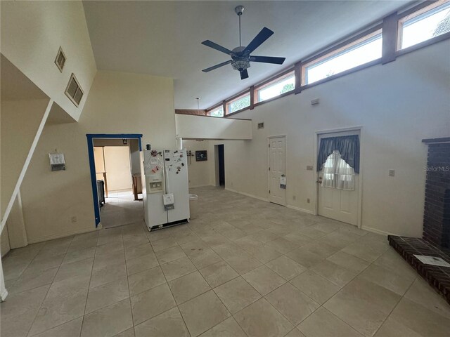 unfurnished living room featuring ceiling fan, light tile patterned floors, and a high ceiling