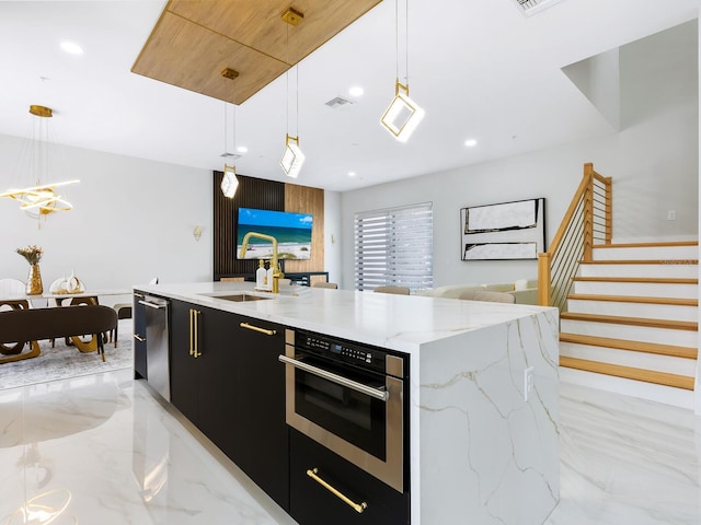 kitchen featuring decorative light fixtures, a center island with sink, visible vents, stainless steel oven, and dark cabinetry