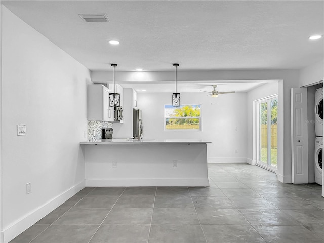 kitchen with decorative backsplash, white cabinets, stacked washer / drying machine, light tile patterned floors, and kitchen peninsula