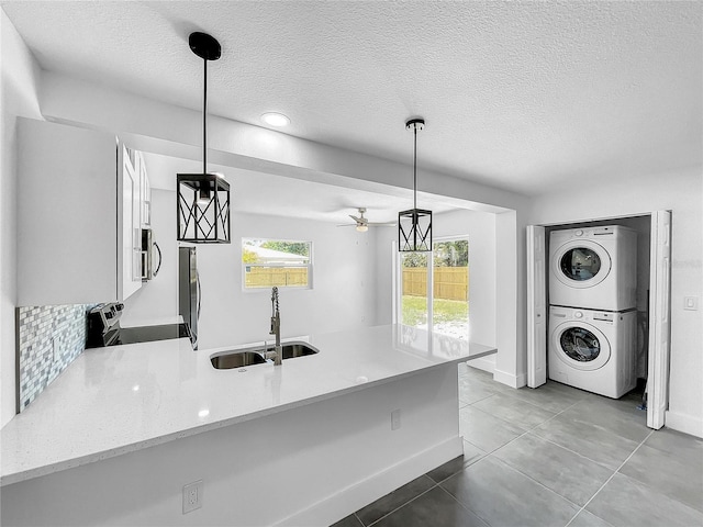 kitchen with stacked washer and clothes dryer, sink, hanging light fixtures, ceiling fan, and stove