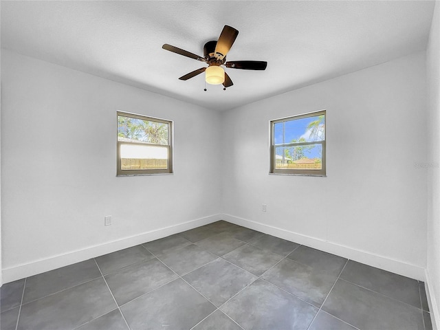 unfurnished room with ceiling fan, a wealth of natural light, and dark tile patterned flooring