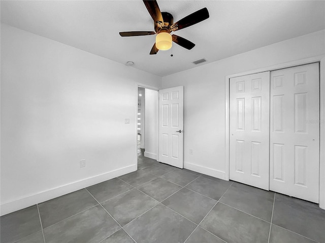 unfurnished bedroom featuring ceiling fan, dark tile patterned flooring, and a closet