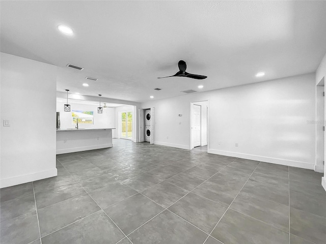 unfurnished living room featuring ceiling fan, tile patterned flooring, sink, and stacked washing maching and dryer