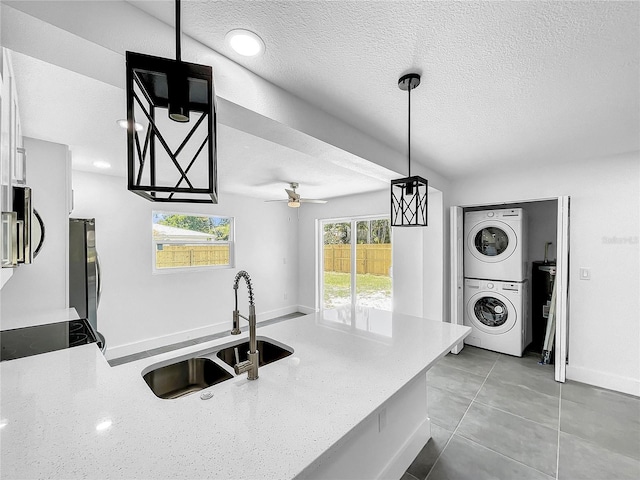 kitchen featuring stacked washer and clothes dryer, sink, a healthy amount of sunlight, and decorative light fixtures