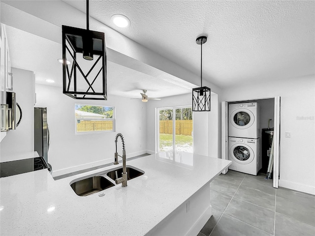 kitchen with a textured ceiling, white cabinets, a sink, appliances with stainless steel finishes, and stacked washer / drying machine
