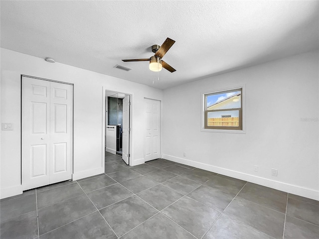 unfurnished bedroom featuring dark tile patterned floors, ceiling fan, and a textured ceiling