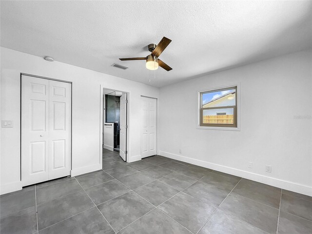 unfurnished bedroom with a textured ceiling, visible vents, dark tile patterned flooring, and baseboards