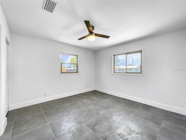 empty room with ceiling fan, plenty of natural light, and dark tile patterned floors