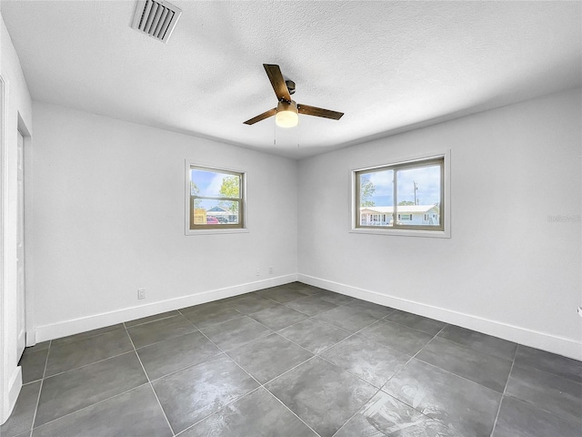 unfurnished room with dark tile patterned floors, baseboards, visible vents, a ceiling fan, and a textured ceiling