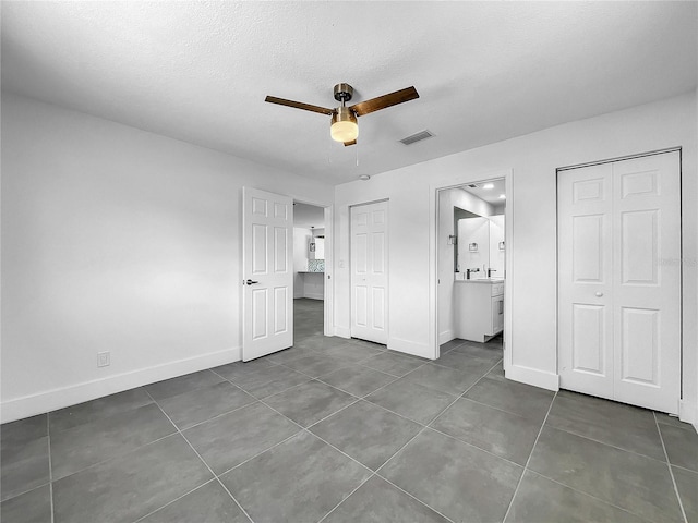 unfurnished bedroom with ceiling fan, dark tile patterned flooring, connected bathroom, and sink