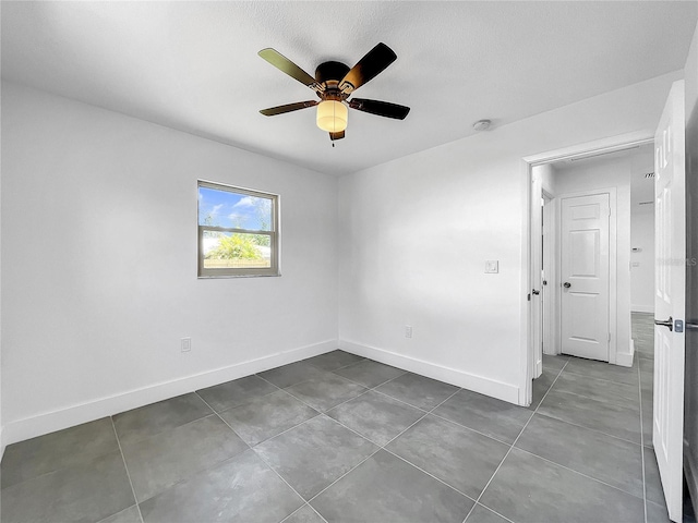 empty room with dark tile patterned flooring, a ceiling fan, and baseboards