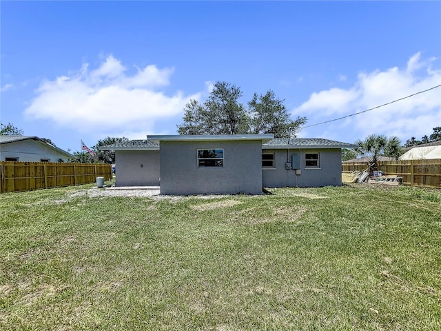 rear view of property featuring a lawn, stucco siding, and a fenced backyard