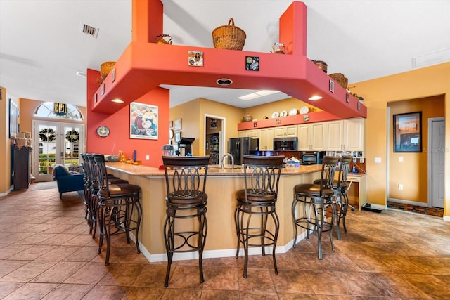 kitchen featuring french doors, black fridge, tile patterned flooring, a kitchen bar, and kitchen peninsula