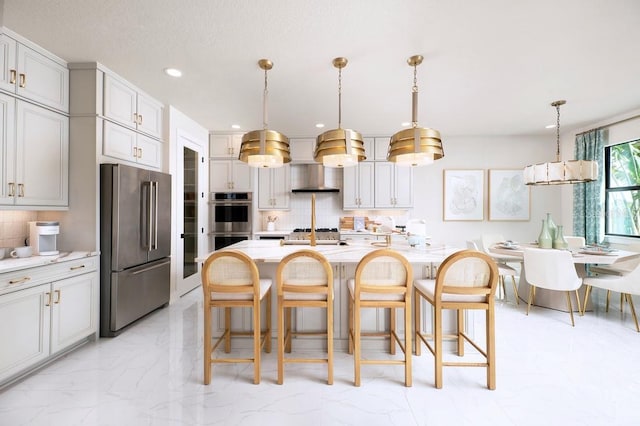 kitchen with wall chimney exhaust hood, hanging light fixtures, light tile patterned floors, a center island with sink, and stainless steel appliances